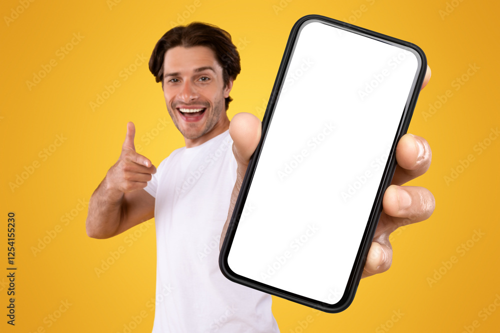 Poster cheerful young guy holding smartphone with white empty screen, pointing at blank display for mobile 