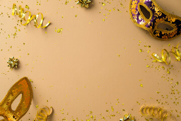 Flat lay gold and purple Venetian masks, golden ribbons, and confetti on a beige background. © photoguns
