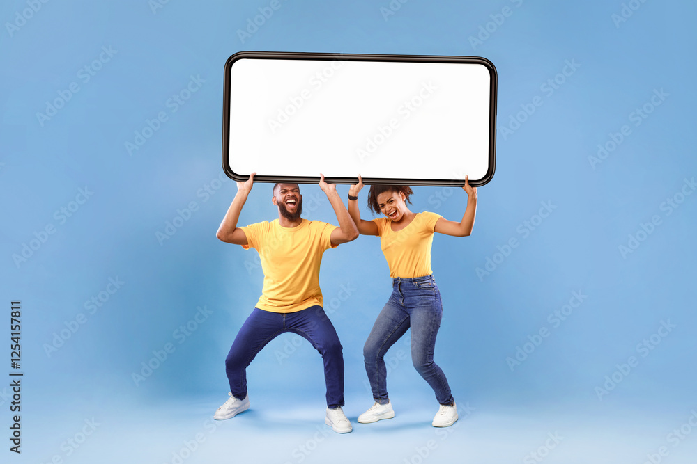Poster millennial african american couple holding huge heavy smartphone with empty screen on blue studio ba