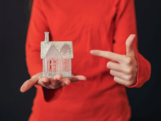 A woman is holding a small glamourous house in her hand and second hand pointing to the object....