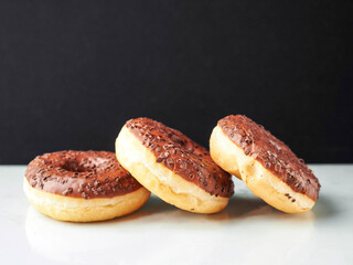 Three chocolate donut with sprinkles on top. The donut is sitting on a white table and dark background. Premium high quality bakery product.