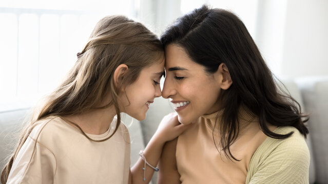 Young loving mother her little daughter share intimate and joyful moment, touch foreheads with eyes closed and smiling, expressing deep bonding and affection. Custody, adoption, family ties, close up