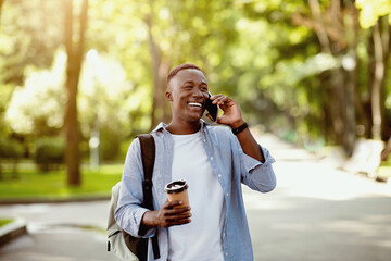 Attractive black guy with takeout coffee communicating on smartphone at urban park, blank space