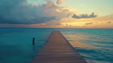 Fototapeta premium A long wooden pier extending into a calm turquoise ocean with a dramatic sunset sky.