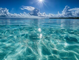 Idyllic tropical ocean scene with clear turquoise water, bright sun, and fluffy clouds.