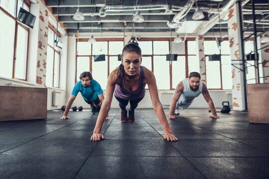Men And Woman Doing Push Ups In The Bright Gym. - Powered by Adobe
