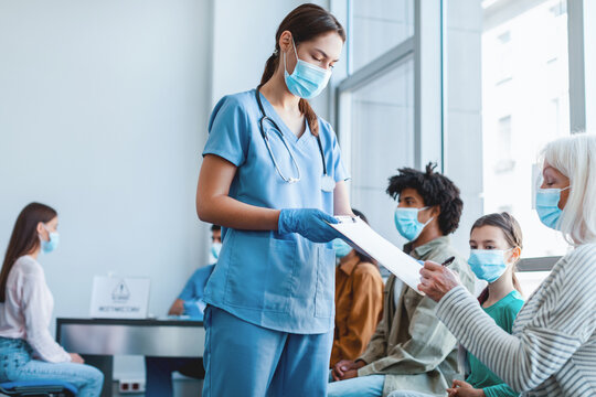 Diverse people waiting in line to get shots or to get tested for flu infection at the hospital. Senior patient signing Informed Consent for Vaccination against pneumonia, influenza or coronavirus