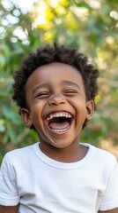 A young boy with curly hair is smiling and laughing. He is wearing a white shirt and is standing in a green field