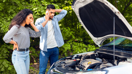 Young arab man calling for help on mobile phone. Upset middle-eastern couple having broken car while countryside trip, calling auto service, looking at engine and touching their heads