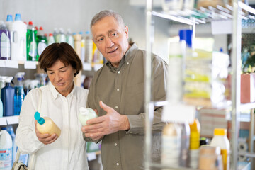 Obraz premium Couple elderly man and woman buyers chooses liquid hand soap in household chemicals store
