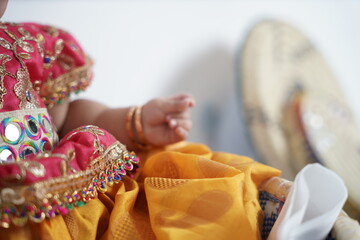 A baby dressed in traditional attire with gold bangles, against a backdrop of woven baskets. A heartwarming and cultural portrait symbolizing heritage, festivities, and cherished traditions.