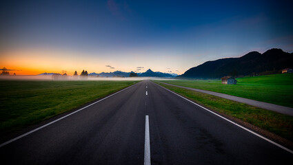 Fototapeta premium Road stretching towards serene mountains under a colorful sunset