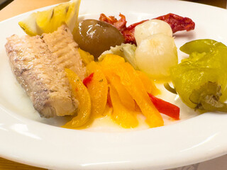 Mediterranean dish with tuna, peppers, olives, and pickles on white plate