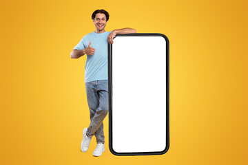 I Recommend. Full body length of cheerful young man leaning on large smartphone with white blank...