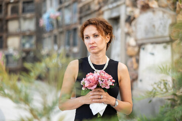 Woman in black dress with bouquet of flowers came to cemetery to honor the memory of a deceased...