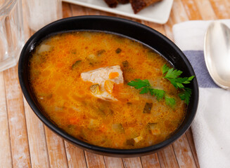 Pickle soup with pearl barley, potatoes, onions, carrots and parsley. Rassolnik in a white plate on a marble background. Traditional dish of Russian cuisine. Top view
