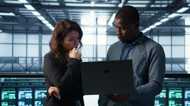 Engineers using laptop in data center, managing server virtualization, running scripts. IT specialists using programming language on notebook in server hub, finetuning network protocols, camera B