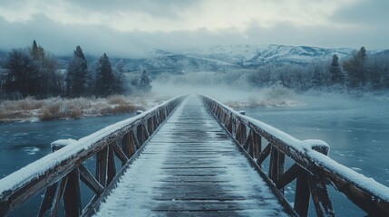 Naklejka premium Snow-Covered Wooden Bridge Extending into Misty Mountains Under Cloudy Sky in Winter Landscape