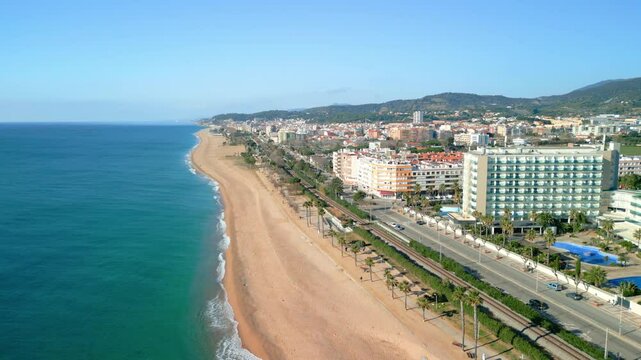 Stunning aerial footage capturing the expansive coastline, sandy beach, and vibrant town of pineda de mar in barcelona&rsquo;s maresme region under a clear blue sky