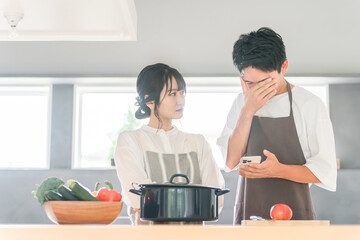 スマホを見ながらキッチンで料理を作る夫婦（レシピサイト・レシピアプリ）
