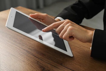 Businesswoman using tablet at wooden table indoors, closeup. Modern technology