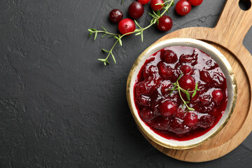 Tasty cranberry sauce in bowl, berries and thyme on black table, top view. Space for text