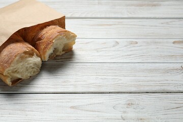 Paper bag with halves of fresh baguette on wooden table, space for text