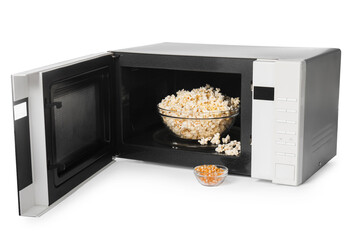 Open microwave oven with bowl of popcorn and kernels isolated on white