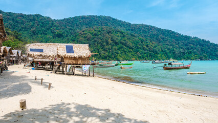 Bright sunshine illuminates the soft sands of Surin Island Thailand as traditional fishing boats gently sway in turquoise waters.