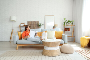 Pretty young woman reading magazine while relaxing on sofa