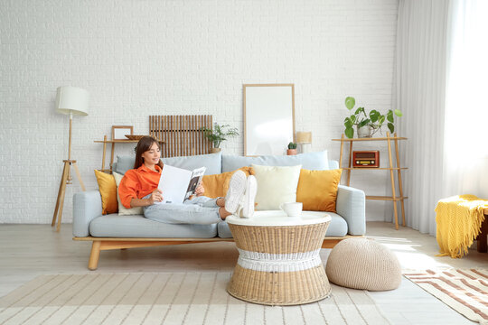 Pretty young woman reading magazine while relaxing on sofa