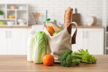 Grocery bag with different fresh products on wooden table in kitchen