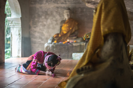 Woman in traditional Northern Thai dress bowing down in front of buddha image in temple