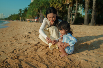 happy toddler baby girl playing sand with mother on sea beach in Pattaya, Thailand