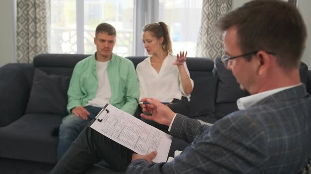 The psychotherapist takes notes as the young couple talks. The woman dismisses irrelevant questions, focusing on key issues while the therapist guides them in resolving communication problems.