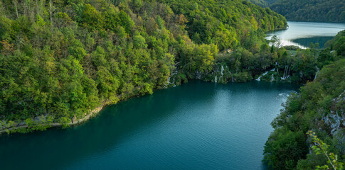 Nature and landscape. Waterfalls in the forest flowing into lakes. Tourists visit famous Plitvice park in Croatia. Mountain streams with clear water. Waterfalls of Plitvice Lakes on a summer day.