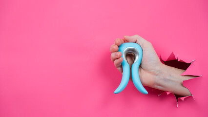 Female hand sticking out of pink paper background with blue curved vibrator sex toy. Copy space. 