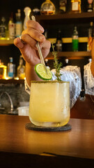 Close-up of a hand carefully placing a lemon slice as decoration on a vintage cocktail served in elegant glassware. The scene highlights meticulous details, vibrant colors, and a warm, blurred backgro