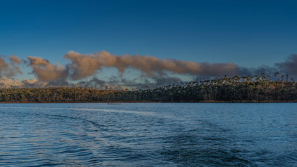 A calm lake. The evening golden hour. Ripples on the blue water. The boat is far away. Green...