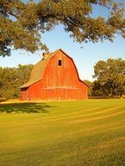 A scenic view of a historic red barn surrounded by golden wheat fields at dusk, creating tranquility.