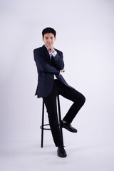 Full body image of young Asian business man sitting in chair on white background