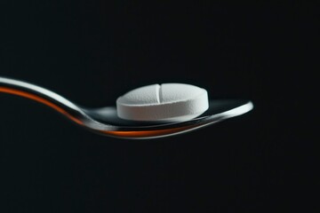 White pill on a spoon for medicinal use on a black background