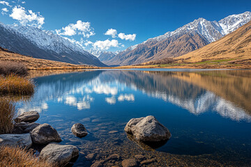 Fototapeta premium Serene mountain lake with crystal clear water reflecting snow-capped peaks and blue sky