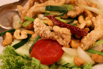 A colorful dish with vegetables, nuts, and crispy meat.