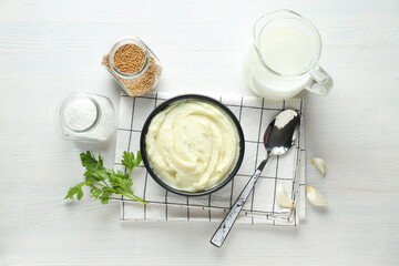 Mashed potatoes in bowl on towel, jug with milk and spices on white background, top view