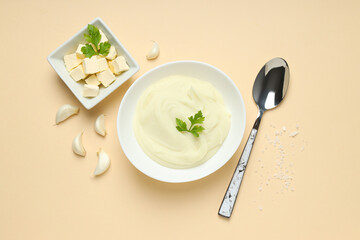 Bowls with mashed potatoes and butter, spoon on beige background, top view