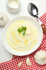 Mashed potatoes in bowl on towel, spoon and garlic on white background, top view