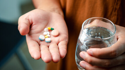 Male hand holding dietary supplement, vitamin C, B, fish oil and holding a glass of water, close-up...