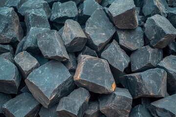 Piles of large, rough black stones collected from a quarry site during daylight hours