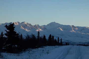 Sun on mountaintop on winte afternoon behind road  in Alaska.